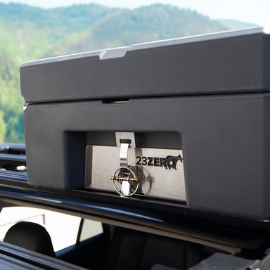 Image of a black 23ZERO storage case mounted on a roof rack with a quick-release pin, against a backdrop of mountains.