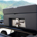 Image of a black 23ZERO storage case mounted on a roof rack with a quick-release pin, against a backdrop of mountains.