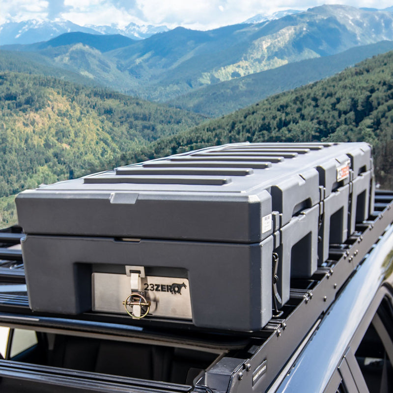 Image of multiple black 23ZERO storage cases secured on a roof rack, with a mountain range in the background.