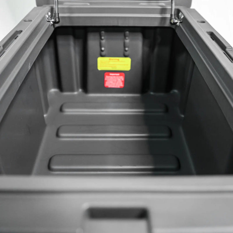 Image of the open interior of a dark gray storage box, showcasing the ribbed bottom and warning labels, direct top view on a white background.