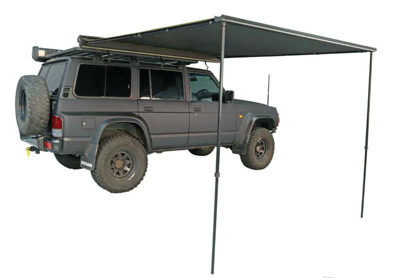 Image of a black Peregrine Awning partially deployed, extending from the side of a dark grey Nissan SUV. The awning is supported by two black poles, providing shade, and is shown against a white background