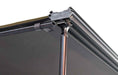 Close-up image of the corner of a deployed Peregrine Awning, showcasing the black support pole, the dark fabric underside, and the robust metal framework. The detailed view highlights the structural components against a clean white background