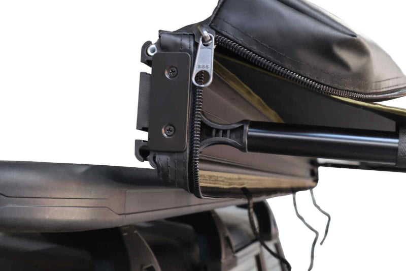 Close-up image of a rolled-up Peregrine Awning attached to a roof rack, highlighting the black zipper with an "SSS" pull tab and the bundled green fabric. The image focuses on the attachment mechanism and the compact storage of the awning against a white background