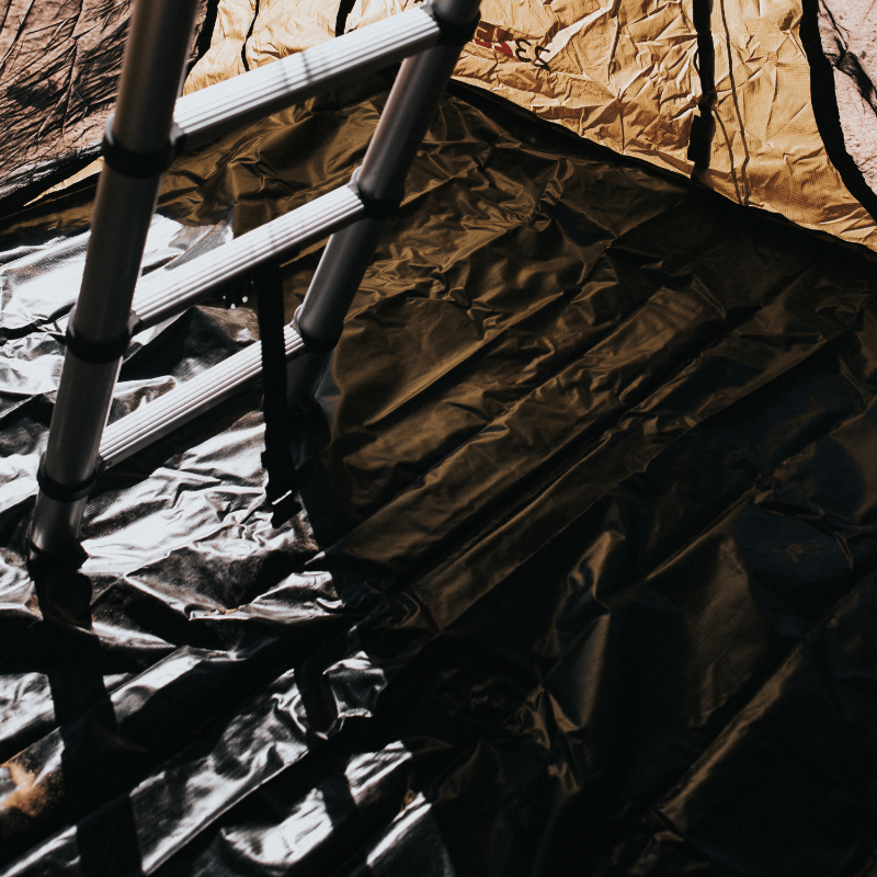 Image of the interior floor of a Walkabout Rooftop Tent Annex, with the shiny black PVC floor liner shown in a close-up view. The aluminum ladder is resting on top of the black floor, leading up to the main tent