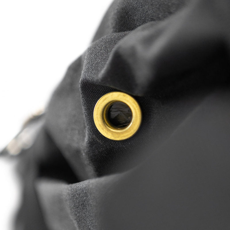 Image of a close-up on a brass grommet embedded in a black fabric, with the material softly folded around it.