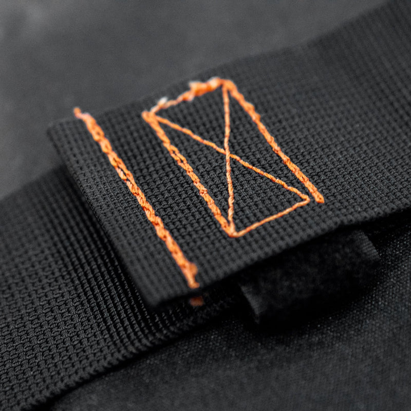 Image showing a close-up of a black fabric strap with reinforced orange stitching, resembling a rectangular box, over another black fabric surface.