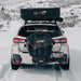 Image of the rear of a white Subaru Crosstrek with a black 23ZERO rooftop tent and a black 23ZERO spare tire storage bag, parked in a snowy landscape.