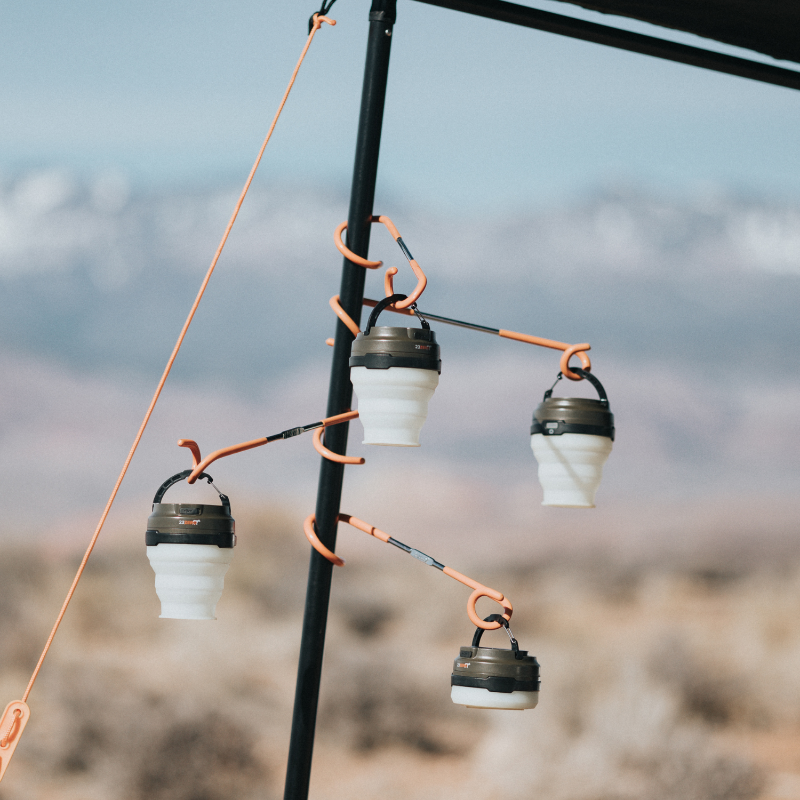 Image of 23ZERO LED solar tent lights hanging from orange lantern hooks on awning pole, angled outdoor campsite view.