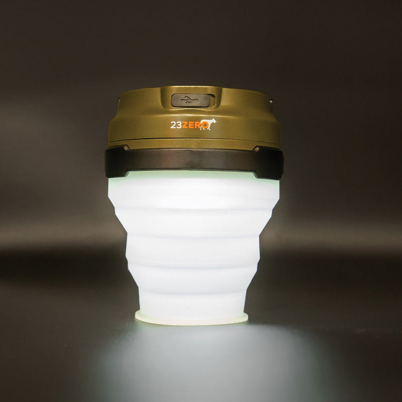 Image of 23ZERO LED solar tent light with collapsible white silicone body and olive green top, front view on dark background.