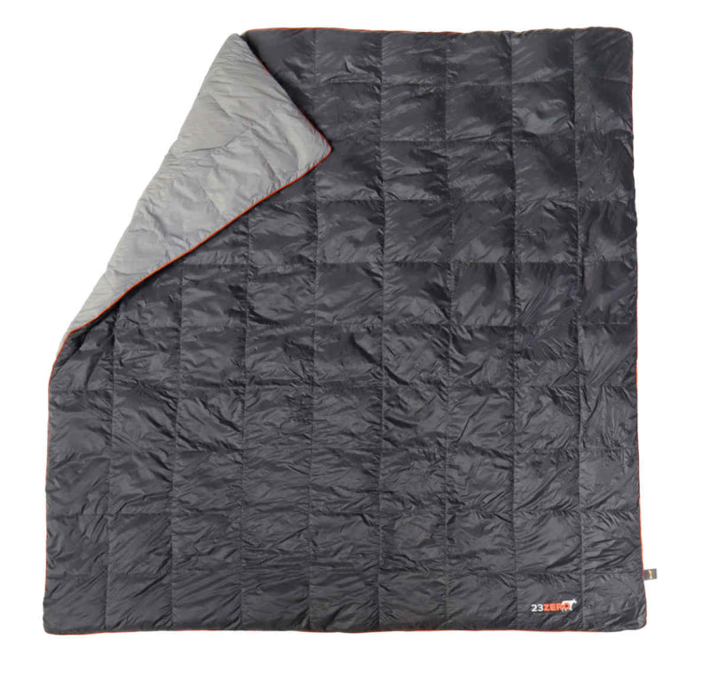Image of a 23ZERO Camping Quilted Blanket, dark grey with a light grey folded corner and orange trim, shown flat on a white background.