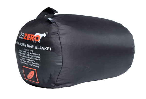 Image of a 23ZERO Duck Down Trail Blanket, horizontally compressed in its black stuff sack with product details printed on the side, displayed on a white background.