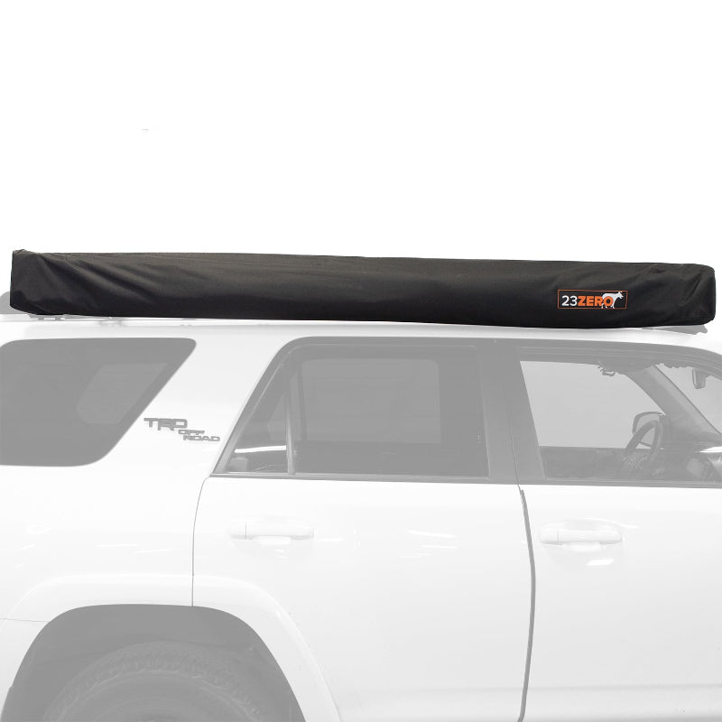 Image of the black 23ZERO Peregrine Pro 270-degree awning in its black transit cover, securely mounted to the roof rack of a white SUV
