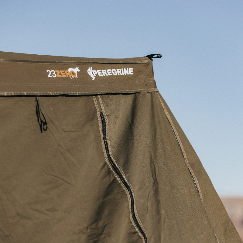 Close-up image of the Peregrine 270 Awning's green fabric with the "23ZERO PEREGRINE" logo visible. The image captures the texture and details of the awning against a blurred outdoor background