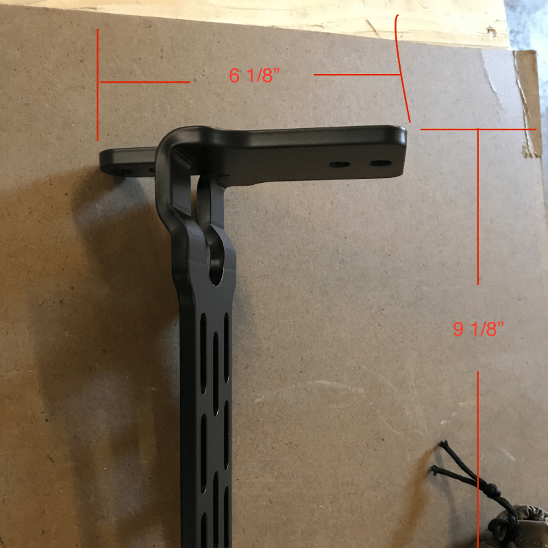 Image of black metal awning mounting bracket with slotted arm and bolt holes, shown with red measurement markings indicating overall length and height, side profile view on a cardboard background.