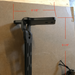 Image of black metal awning mounting bracket with slotted arm and bolt holes, shown with red measurement markings indicating dimensions, side profile view on a cardboard background.