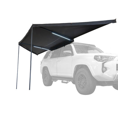 Image of a Peregrine PRO 180 Awning partially deployed with LED lights on, angled front and side view. The black fabric awning is mounted to the side of a white SUV, which is ghosted out in the background
