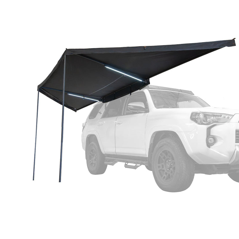 Image of a Peregrine PRO 180 Awning partially deployed with LED lights on, angled front and side view. The black fabric awning is mounted to the side of a white SUV, which is ghosted out in the background