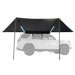 Image of a Peregrine PRO 180 Awning fully deployed with LED lights on, showing a straight side view. The black fabric awning is mounted to a white SUV, which is ghosted out in the background