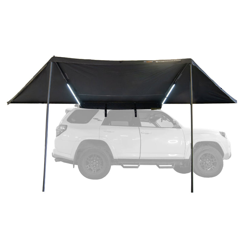Image of a Peregrine PRO 180 Awning fully deployed with LED lights on, showing a straight side view. The black fabric awning is mounted to a white SUV, which is ghosted out in the background