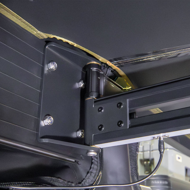 Image of a close-up detail of the Peregrine PRO 180 Awning bracket and mounting hinge. The photo shows the heavy-duty black metal bracket and bolts, highlighting the awning's sturdy connection to the vehicle