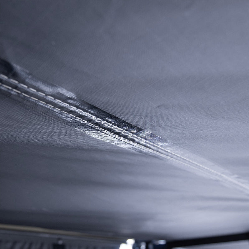 Image of a close-up detail of the Peregrine PRO 180 Awning's black fabric, highlighting the double-stitched seam for durability. The photo shows the robust stitching on the underside of the awning