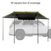 Image of a 23ZERO Peregrine 180 Compact Awning fully deployed from the rear of a vehicle, providing 45 square feet of coverage. The awning's green fabric with a black underside is supported by black poles, creating a shaded area behind a white vehicle