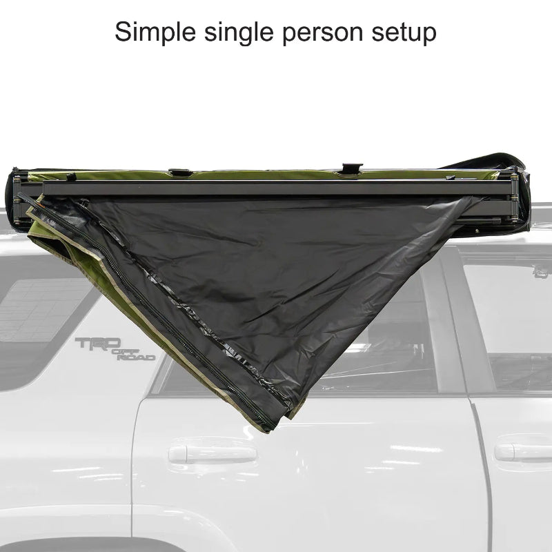 Image of a 23ZERO Peregrine 180 Compact Awning partially unzipped from its cover, with the green fabric and black underside beginning to unfurl. The awning's internal structure and the end of the transit cover are visible, mounted on a vehicle's roof rack