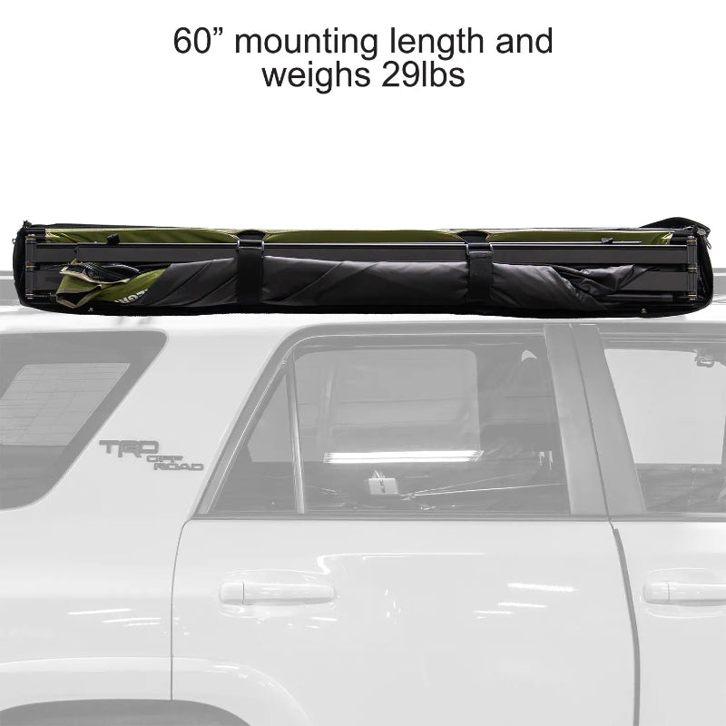 Image of a 23ZERO Peregrine 180 Compact Awning partially rolled up and secured with black straps on a vehicle's roof rack. The green fabric with a black underside is visible, showing the awning in its compact, travel-ready state