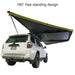 Image of a 23ZERO Peregrine 180 Compact Awning fully deployed in a 180-degree free-standing design from the rear and side of a white SUV. The green fabric with a black underside provides extensive shade, showcasing its wide coverage