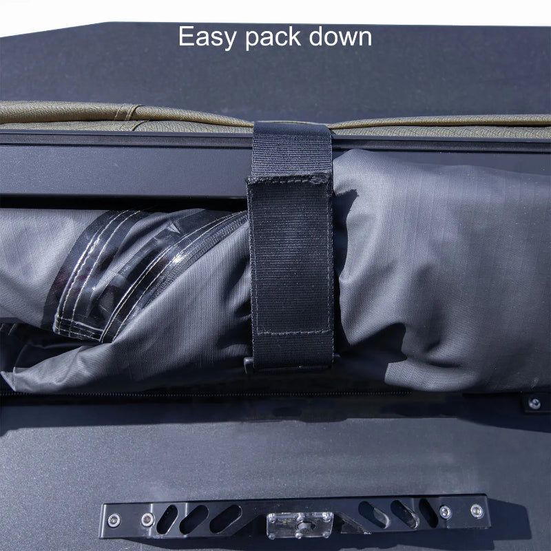 Image of a 23ZERO Peregrine 180 Compact Awning being packed away, with a black strap holding the rolled-up green fabric and black underside against the awning frame. The product is shown from a close-up, top-down view