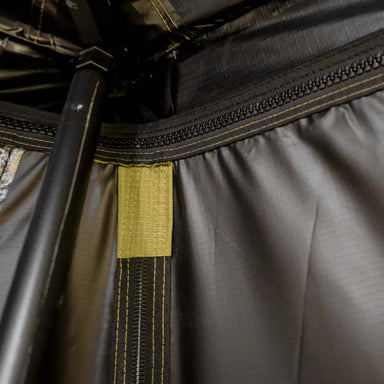 Close-up image showing the interior of an awning with a black zipper, olive green fabric with dark stitching, and a supporting pole