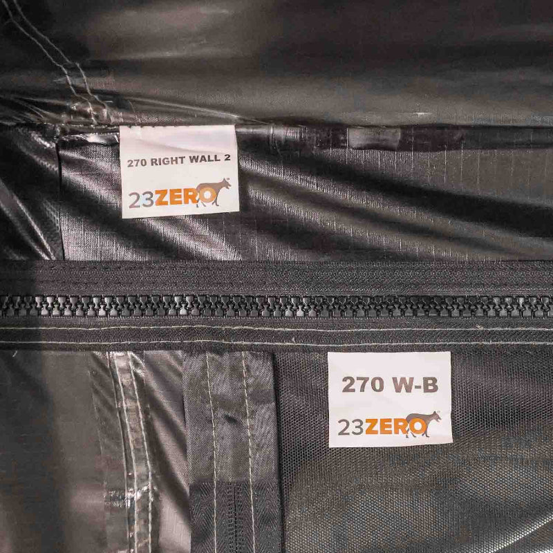 Close-up image of two labels on dark fabric, one reading '270 RIGHT WALL 2' and the other '270 W-B', both with the '23ZERO' logo, next to a black zipper