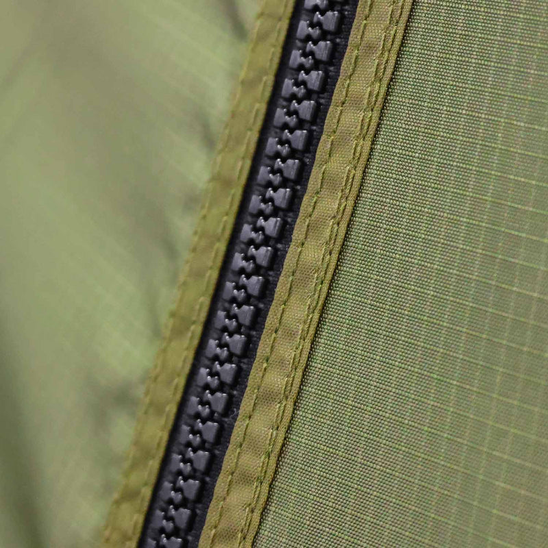 Close-up image of a black heavy-duty zipper on olive green ripstop fabric, showing the texture and stitching in detail