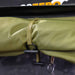 Image of a rolled-up Peregrine Awning, secured with a strap and a black toggle. The green ripstop fabric has a diamond pattern, and a black D-ring is visible below the toggle