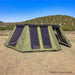 Image of a large, green 23ZERO Peregrine wall kit fully deployed, creating an expansive enclosed space in a dry, grassy landscape. The structure features multiple large mesh windows and is attached to an awning, with hills and a clear blue sky in the background