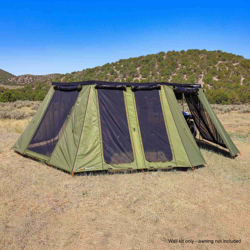 Image of a large, green 23ZERO Peregrine wall kit fully deployed, creating an expansive enclosed space in a dry, grassy landscape. The structure features multiple large mesh windows and is attached to an awning, with hills and a clear blue sky in the background