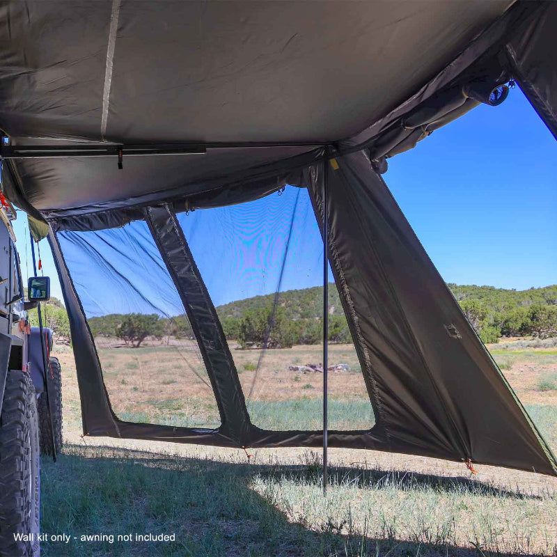 Image of a large, dark green 23ZERO Peregrine wall kit, featuring a black mesh window, attached to an awning. The view is from inside the awning looking out at a dry, grassy landscape with rolling hills in the background
