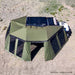 Image of a large, green 23ZERO Peregrine wall kit attached to a Peregrine Awning and a vehicle, viewed from an aerial perspective. The wall kit is fully deployed with mesh screen windows, creating an enclosed space in a dry, grassy landscape