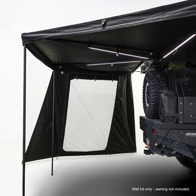 Image of an OVS Nomadic 270-degree awning with two black walls deployed, one with a large white panel, LED lights underneath, attached to the rear of an off-road vehicle, with a note 'Wall kit only - awning not included' at the bottom, all on a white background