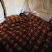 Image of an orange, blue, and black plaid sleeping bag and pillow inside a tent, with a white quilted mattress and tent fabric visible in the background.