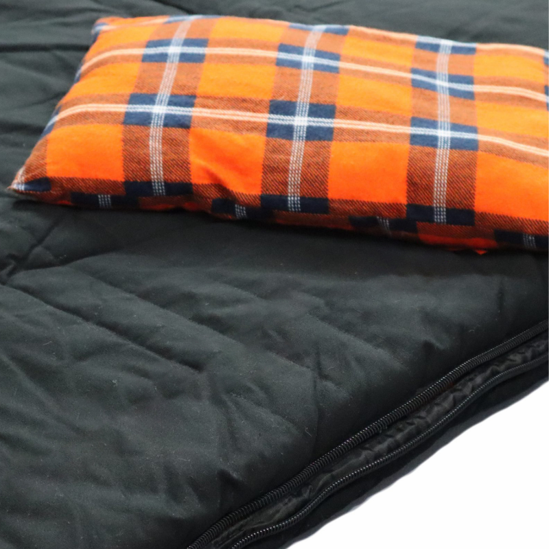 Image of a small rectangular pillow with orange, blue, and white plaid fabric, resting on a black quilted sleeping bag with a visible zipper.