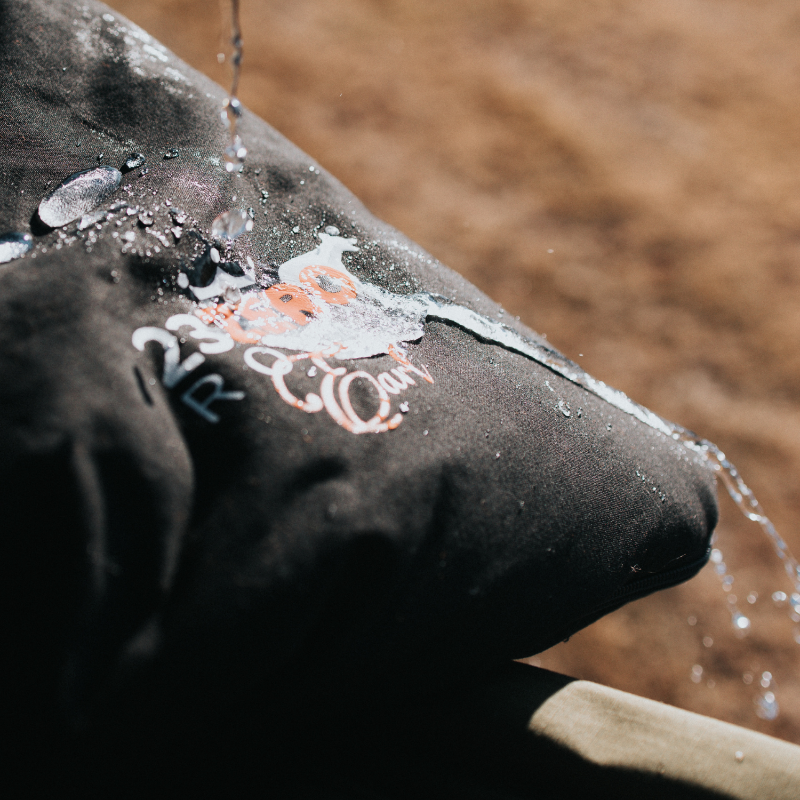 Image of water splashing and beading on a dark, possibly waterproof, fabric surface with "23ZERO" logo text, indicating water resistance.