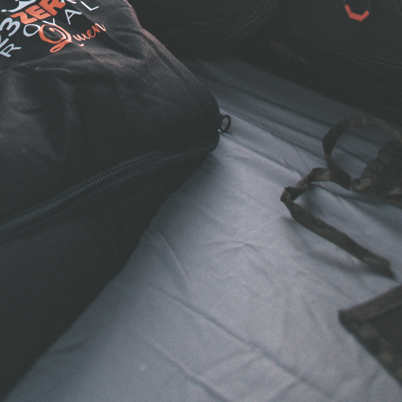 Image of grey fitted mattress sheet installed inside rooftop tent with sleeping bag and straps, close-up angled interior view in low light setting.