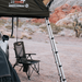 Image of a dark green roof top tent deployed from a vehicle, with a telescopic ladder extended to the ground and a black camping chair positioned underneath, all set in a desert landscape.
