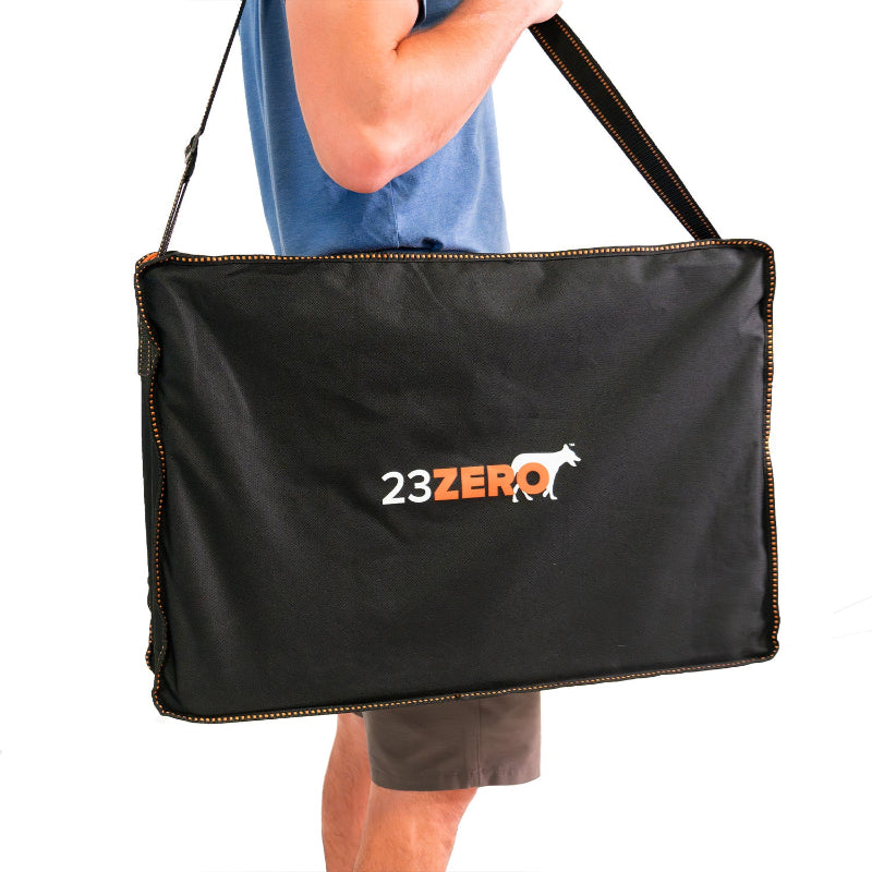 Image of 23ZERO camping table carry bag with shoulder strap and orange trim, black fabric rectangular case shown over shoulder on white background.