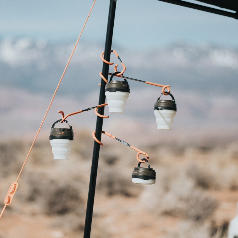 Image of 23ZERO universal 2-way lantern hooks with orange coated steel arms holding camping lights on tent pole, outdoor campsite view.