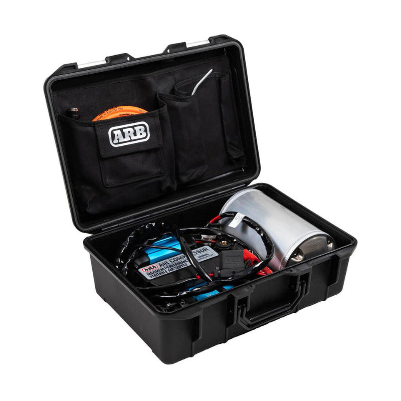 Image of an open black ARB hard case revealing a portable air compressor kit, including a black and blue compressor unit, a cylindrical silver air tank, and an orange air hose neatly stored in the lid's pocket, all against a white background