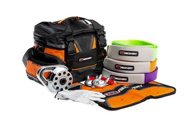 Image of an ARB Premium Recovery Kit on a white background, featuring a black and orange recovery bag, tree trunk protector strap, two bow shackles, a snatch block, and leather gloves. All items are laid out in front of the bag for a clear view