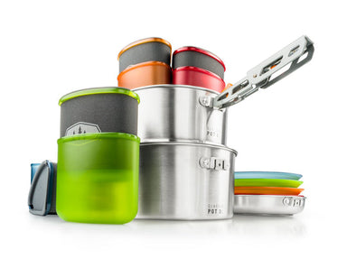 Image of GSI Outdoors Pinnacle Camper Cookset with nesting pots, frying pan, plates, insulated mugs, and pot gripper, stacked and arranged on a white background.