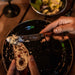 Image of stainless steel serrated table knife with wooden handle spreading soft cheese onto sliced bread, close-up dining scene with plate and salad in background.